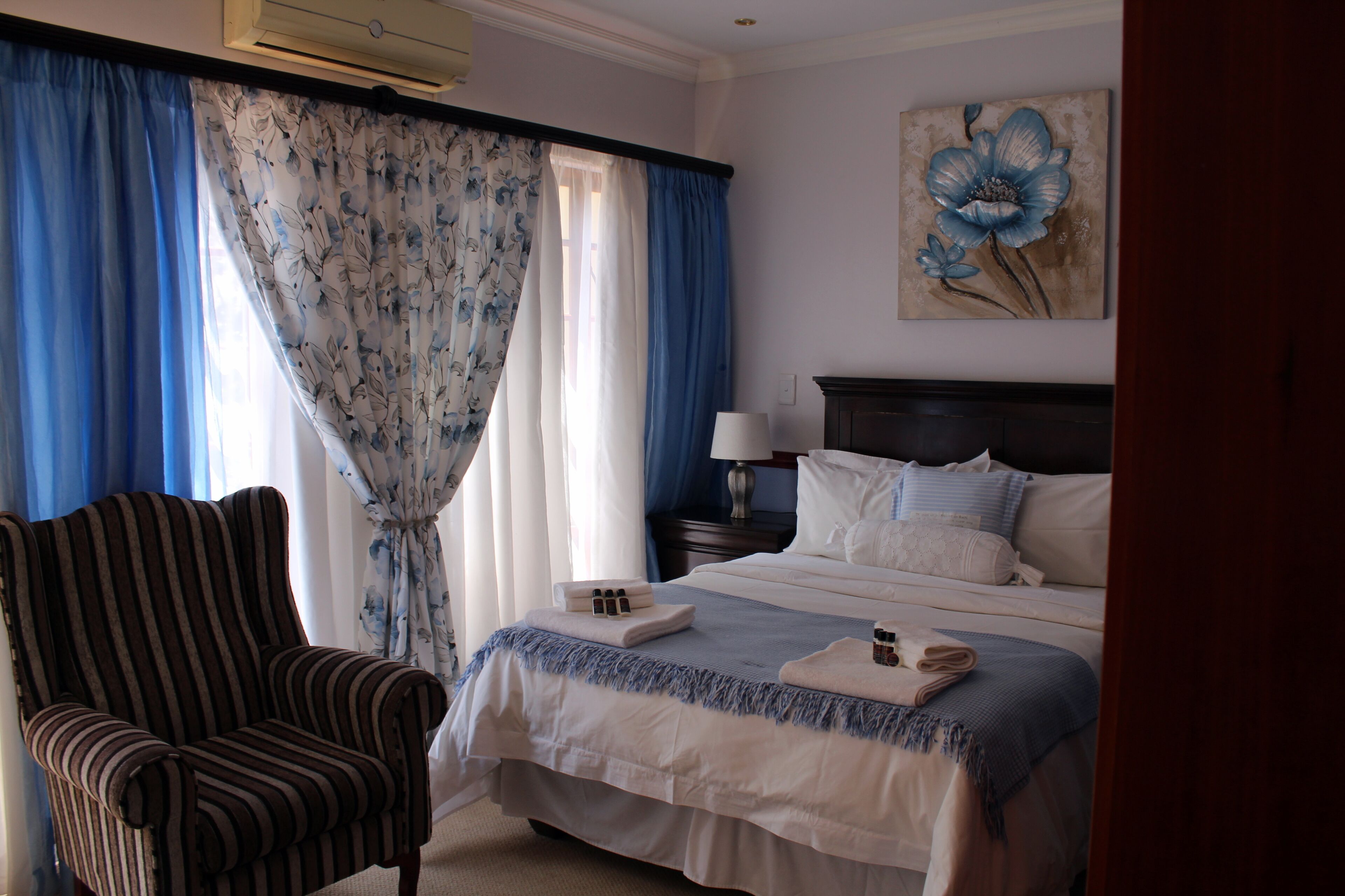 Una habitación de hotel con una cama, una silla, un cuadro y cortinas.