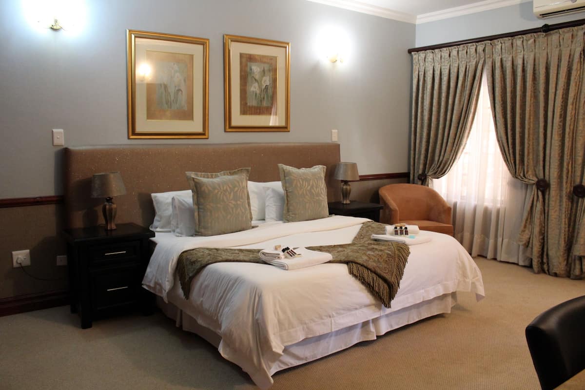 A hotel room with a large bed, two bedside tables, a chair, and a window with curtains.