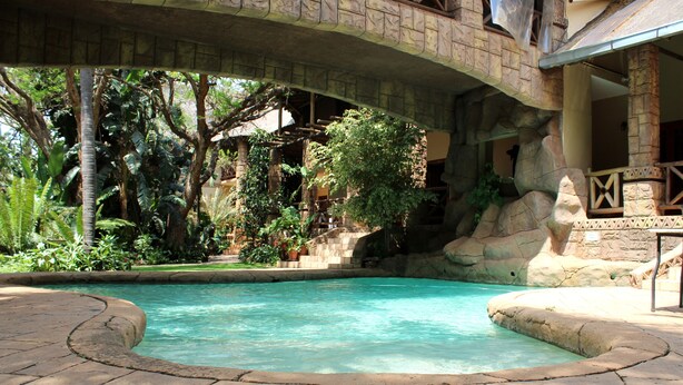 A pool area with a stone bridge, lush greenery, and a stone wall. - Prinshof Manor Guesthouse (Pretoria)