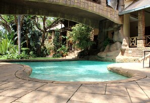 Un área de piscina con un puente de piedra, abundante vegetación y un muro de piedra.