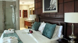 A hotel room with a bed, a bathroom, and a large framed picture on the wall. - Prinshof Manor Guesthouse (Pretoria)