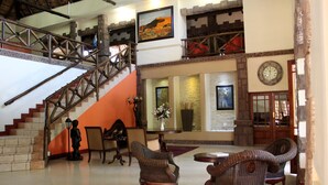 A spacious lobby with a staircase, wicker furniture, a clock, and a fireplace. - Prinshof Manor Guesthouse (Pretoria)