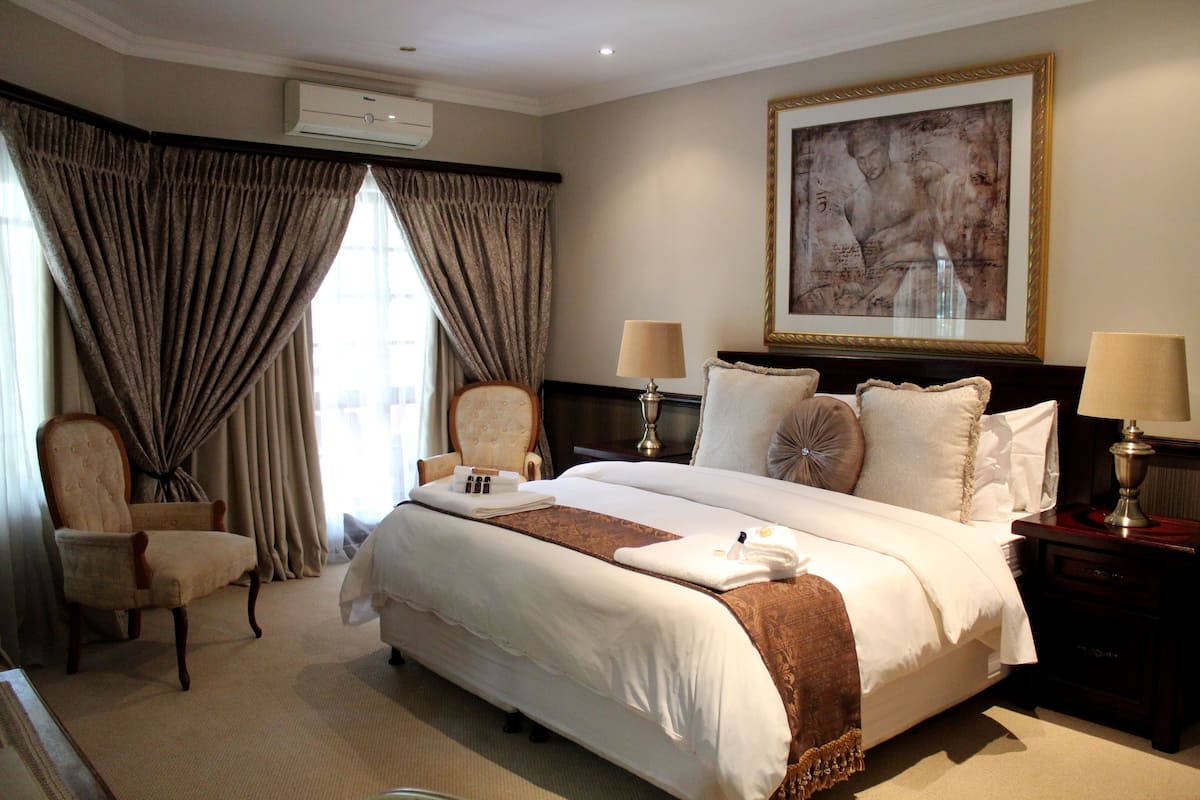 A hotel room with a large bed, two bedside tables with lamps, a chair, and a large framed artwork on the wall.