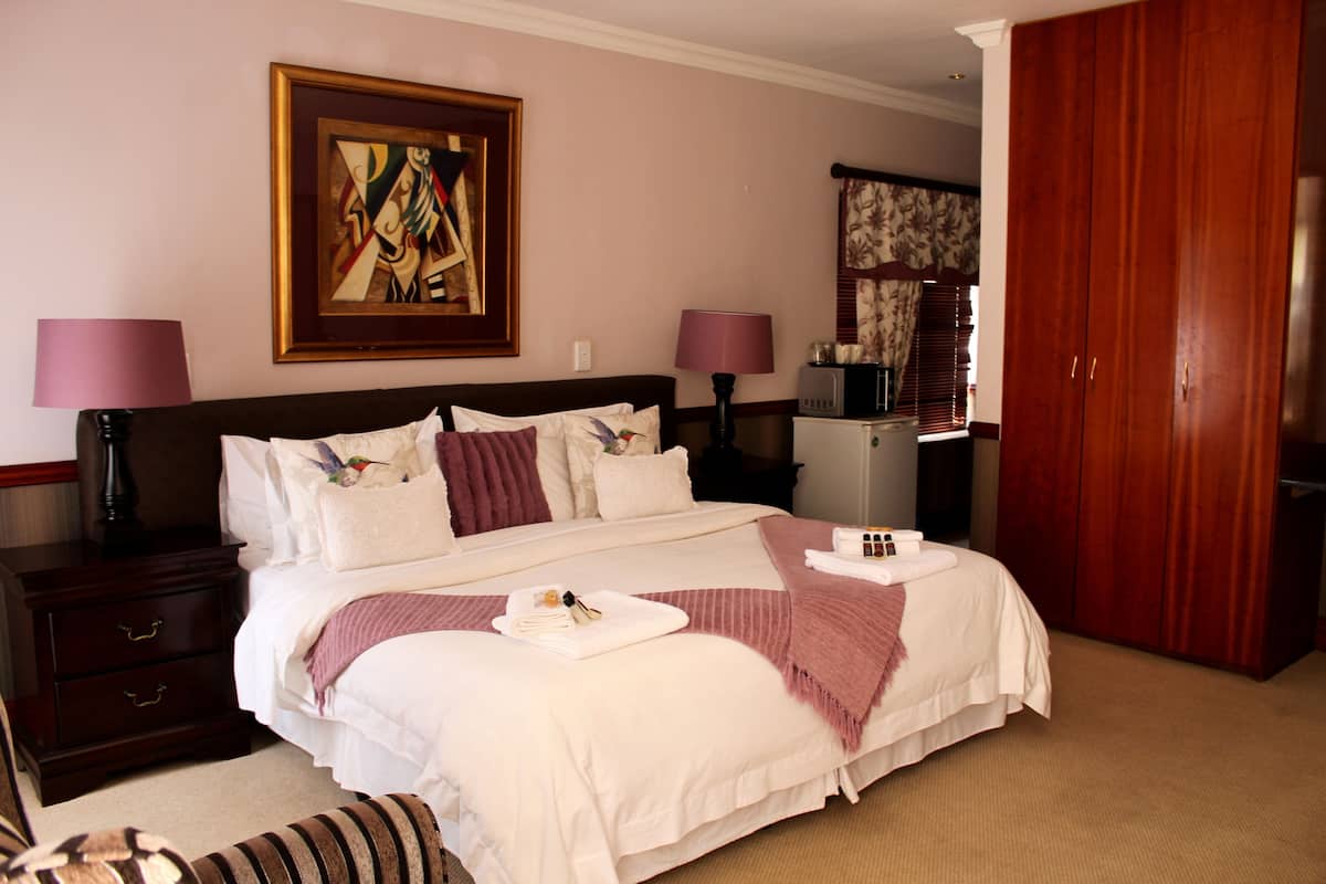 A hotel room with a large bed, two bedside tables with lamps, a wooden wardrobe, and a painting on the wall.