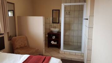 Habitación de hotel con cama, una silla, baño con lavamanos, espejo y ducha.