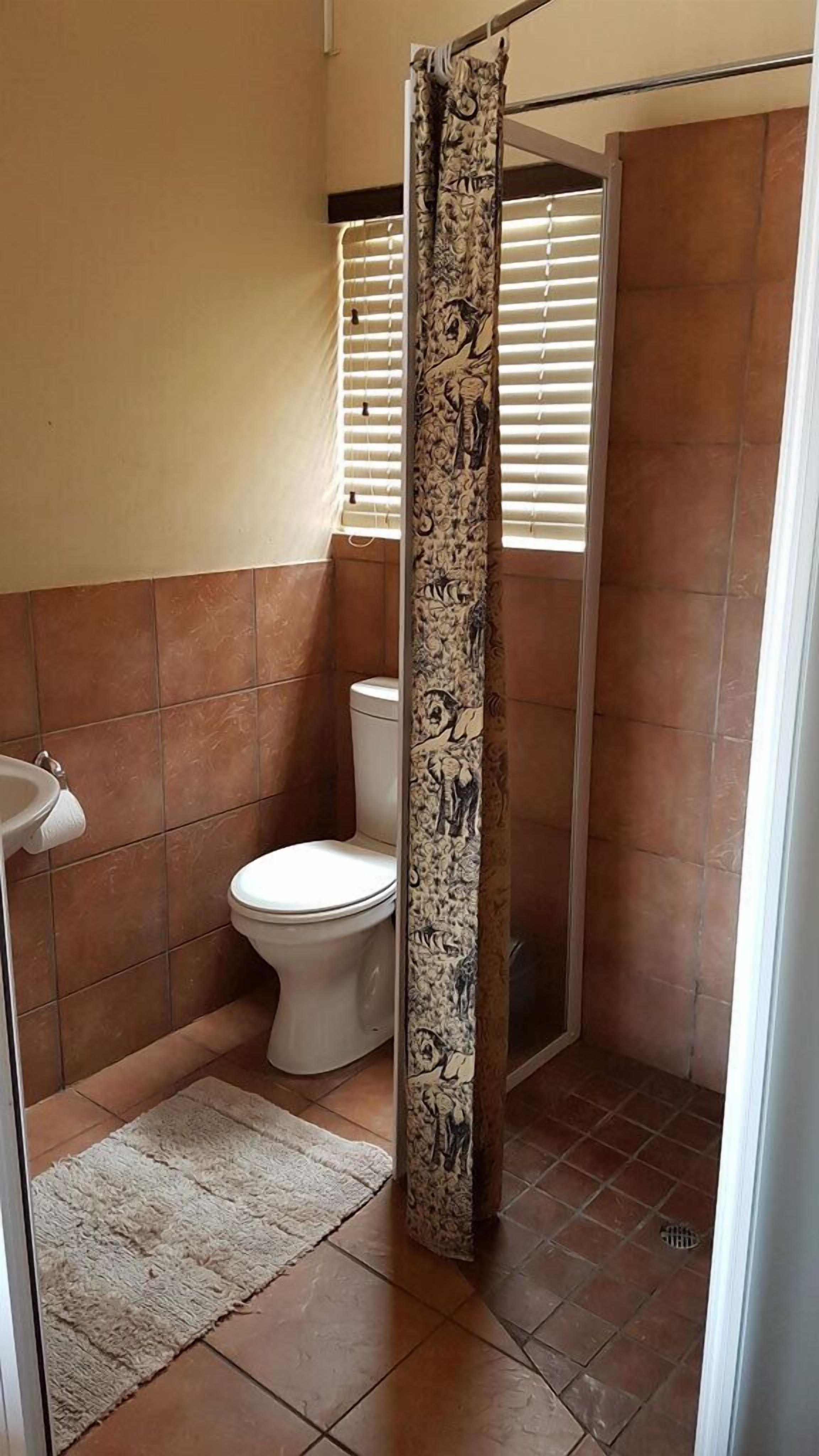 A bathroom with a shower curtain, toilet, sink, and tiled floor.