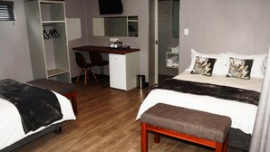A hotel room with two beds, a desk, a chair, a wardrobe, and a shower area. - Tsessebe Guesthouse (Bloemfontein)