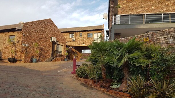 A courtyard with brick buildings, a red fire hydrant, and various plants. - Tsessebe Guesthouse (Bloemfontein)