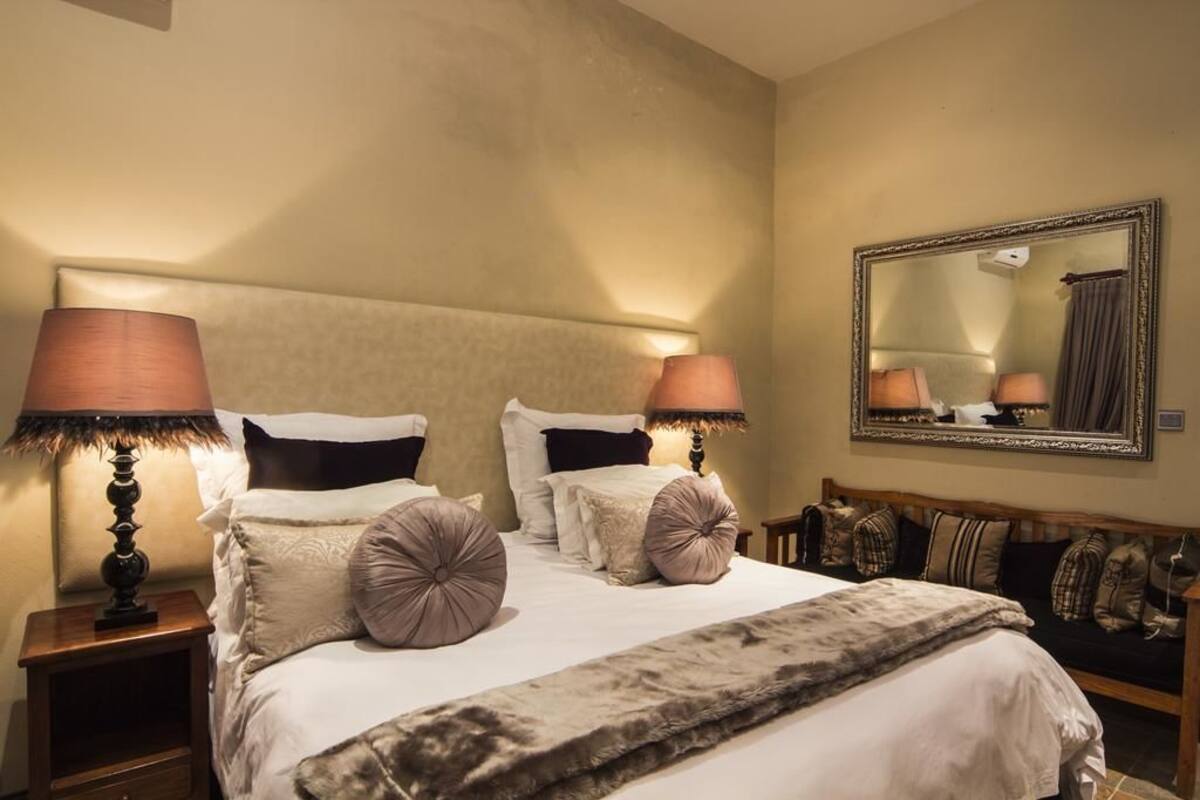 Un lit bien fait, recouvert d’une couverture moelleuse, avec deux lampes de chevet et un grand miroir accroché au mur.