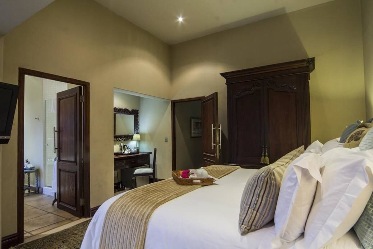 Une chambre d’hôtel avec un grand lit, une armoire en bois et un bureau avec une chaise.