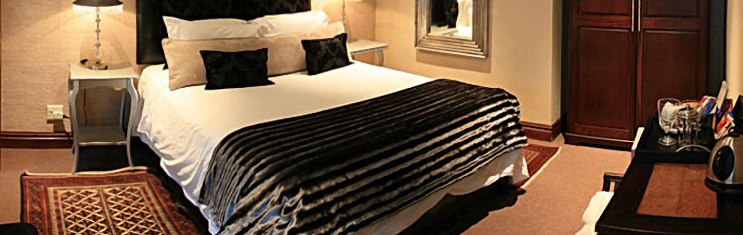Una habitación de hotel con una cama bien hecha, una mesita de noche con una lámpara, una pequeña mesa con un jarrón de flores y un armario.