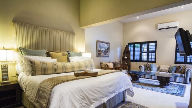 Ein geräumiges Schlafzimmer mit einem großen Bett, einer Sitzecke mit Sofa und Sesseln und Blick ins Freie durch die Fenster.