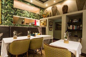 Ein Restaurant mit runden Tischen, Korbstühlen und einer grünen Wand aus Blättern.