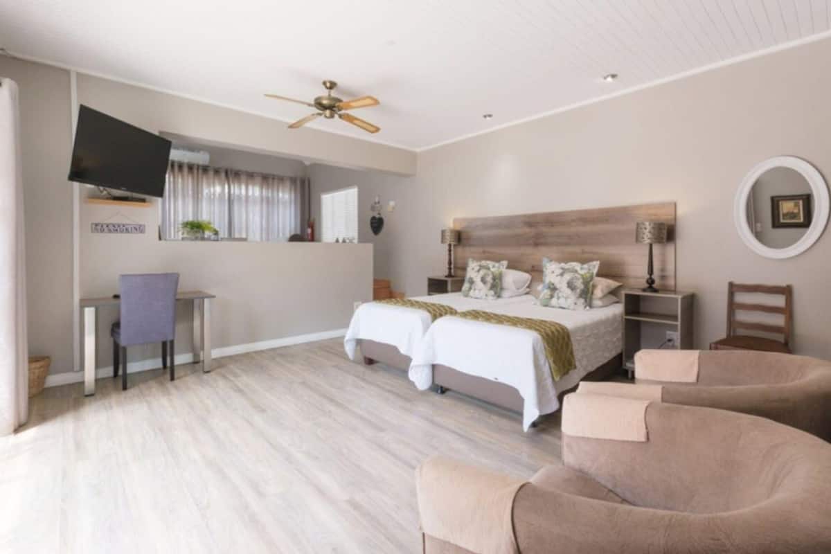 A bedroom with two beds, a desk, a chair, a TV, and a ceiling fan.