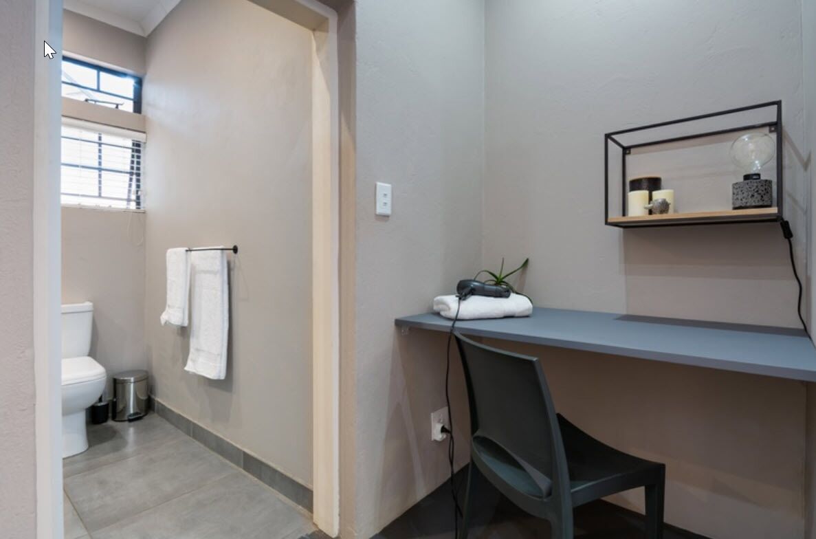 Un baño con inodoro, lavamanos, toallero y estante con artículos de tocador.