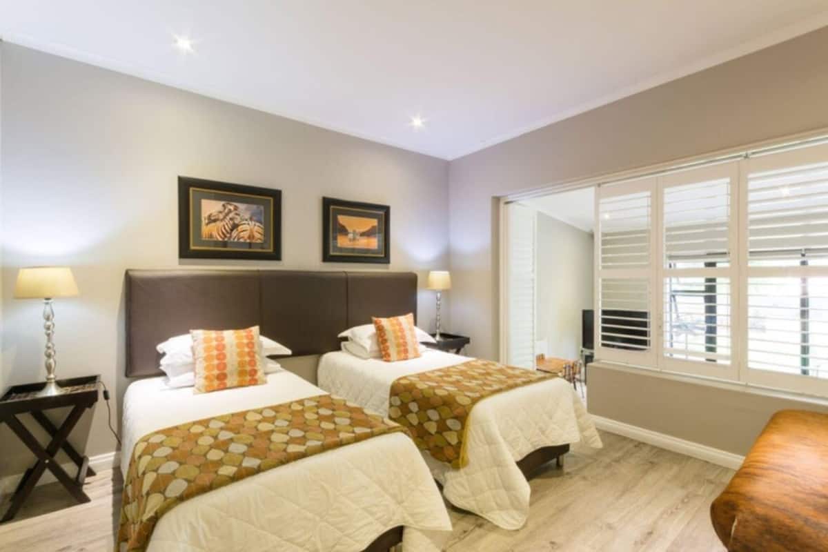 A hotel room with two beds, a large window with blinds, and a framed picture on the wall.