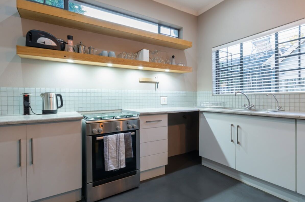 A modern kitchen with white cabinets, a stainless steel stove, and a window with blinds.