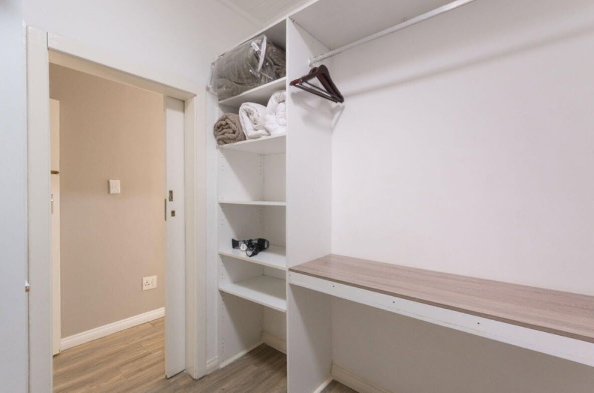 A walk-in closet with open shelves, a hanging rod, and a wooden bench.