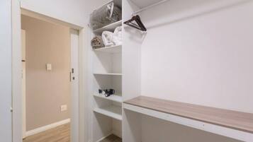 A walk-in closet with open shelves, a hanging rod, and a wooden bench.