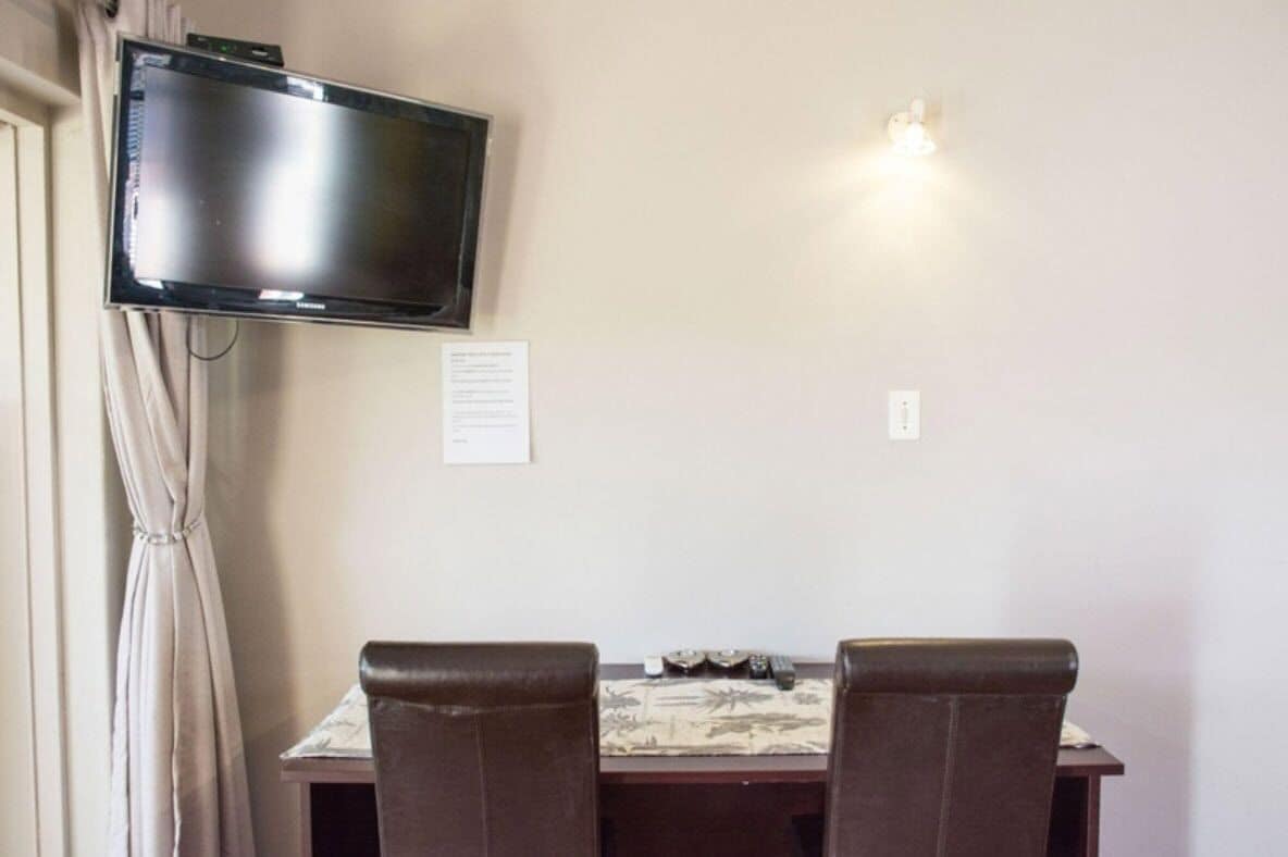 A room with a flat-screen TV mounted on the wall, a table with chairs, and a small light fixture above the table.