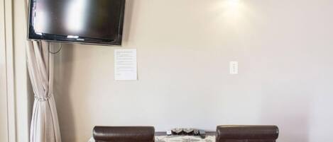 A room with a flat-screen TV mounted on the wall, a table with chairs, and a small light fixture above the table.