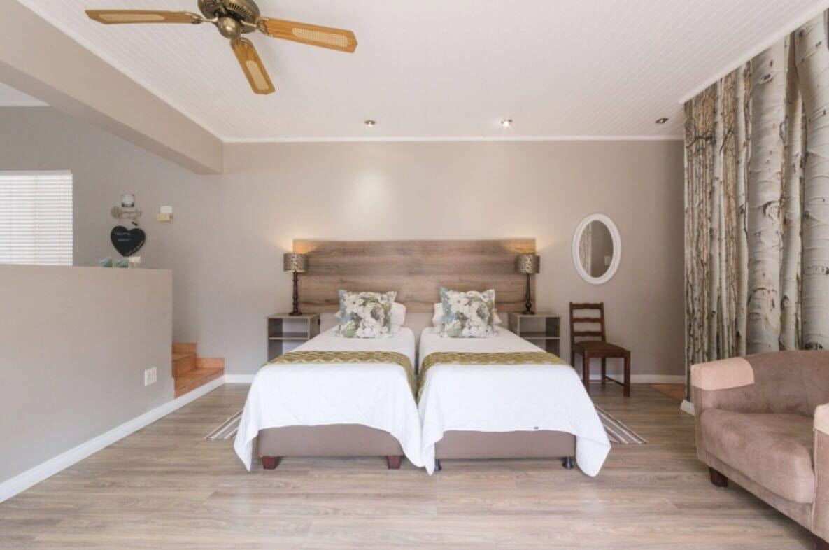 Une chambre avec deux lits, un ventilateur de plafond, une table de chevet, une chaise et un canapé.