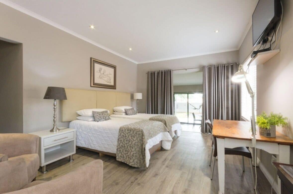 A hotel room with a bed, bedside table, lamp, chair, desk, and a TV.