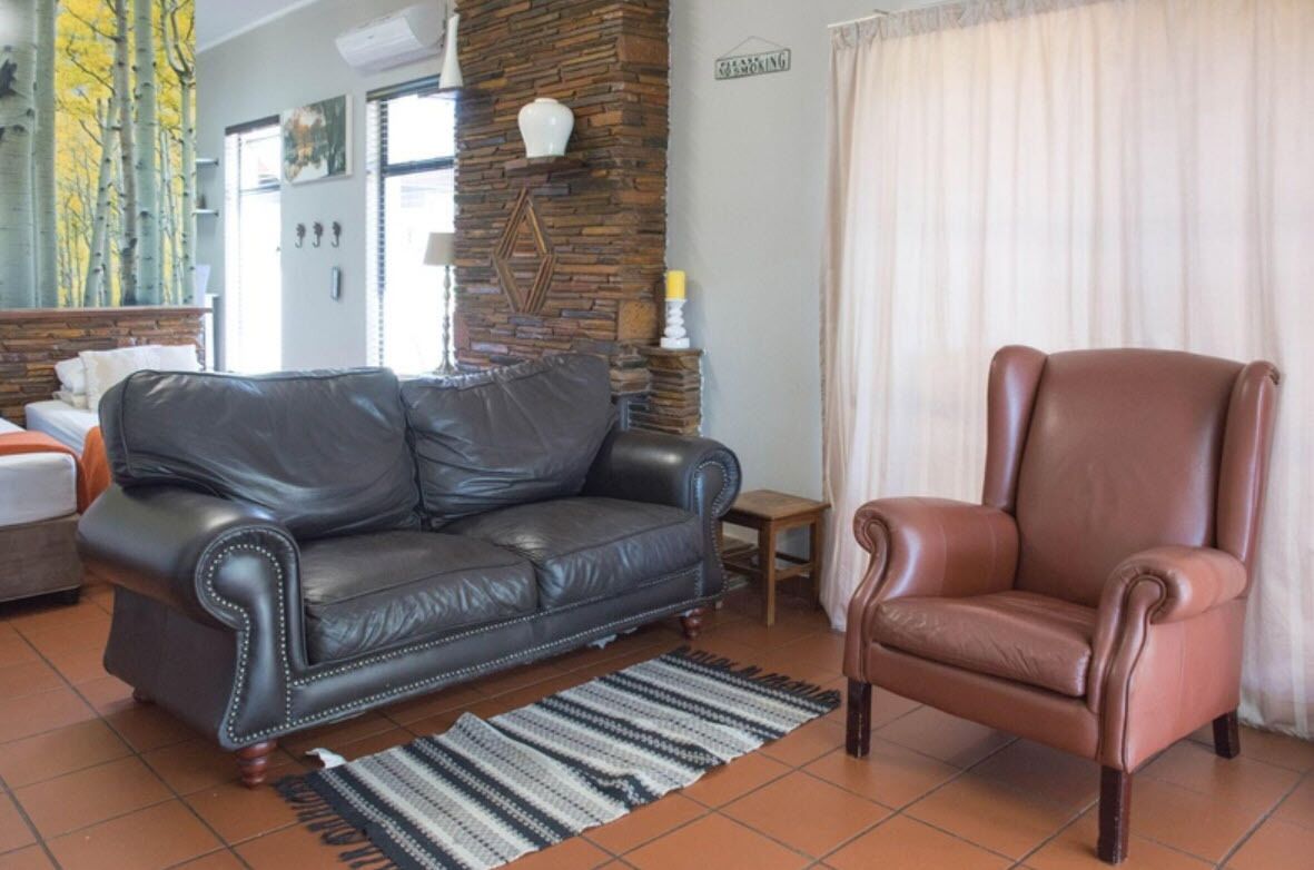 A living room with a black leather sofa, a brown leather armchair, a patterned rug, a small wooden table, and a stone pillar with a decorative item.