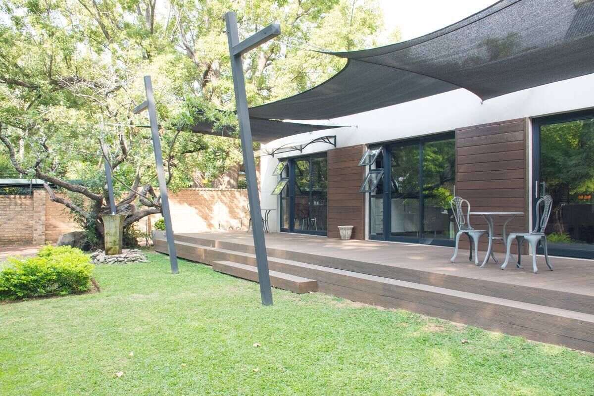 Un patio moderno al aire libre con una zona de estar cubierta, una terraza de madera y un árbol grande.