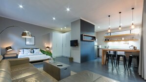 Ein modernes Wohnzimmer mit einer Couch, einem Couchtisch und einem Bett. Es gibt eine Küchenzeile mit einem Esstisch und Barhocker.