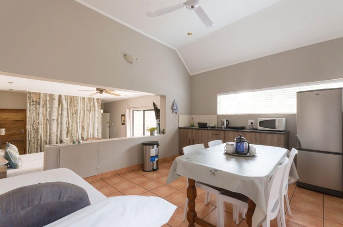 A compact room with a bed, a dining table with chairs, a kitchen area with a refrigerator, microwave, and kettle, and a ceiling fan.