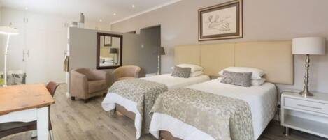 A hotel room with two beds, a sitting area with a chair, a desk, and a lamp.