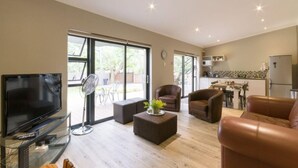 Ein modernes Wohnzimmer mit Flachbildfernseher, Ledersofas, einem Couchtisch und einem Essbereich mit Küche im Hintergrund.