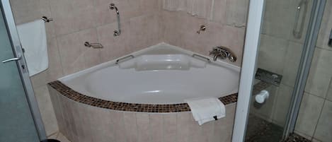 A bathroom with a large bathtub, a shower area, and a tiled floor.