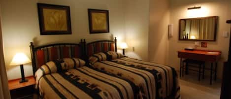 A hotel room with two beds, a desk, and a chair. There are two lamps on the nightstands.