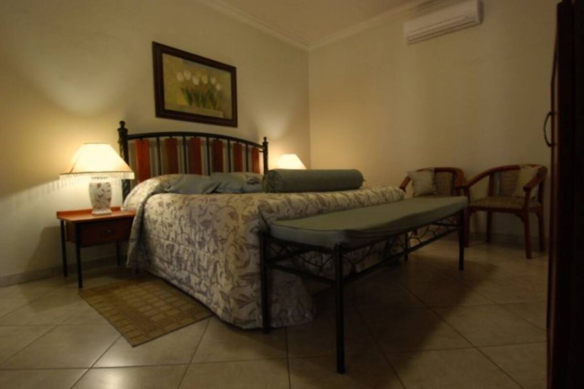 A bedroom with a bed, two bedside tables with lamps, a chair, and a painting on the wall.