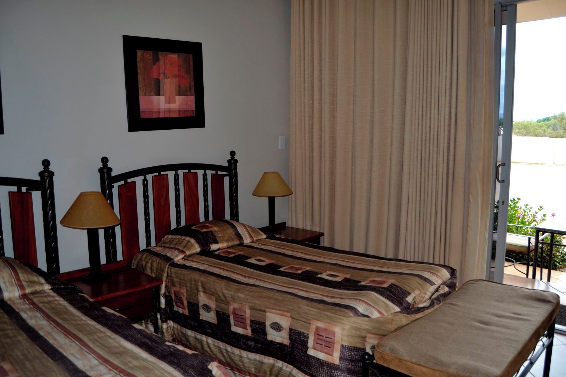 A hotel room with a bed, two bedside lamps, a window with curtains, and a painting on the wall.