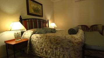 A bedroom with a bed, two bedside lamps, a framed picture on the wall, and an air conditioning unit.