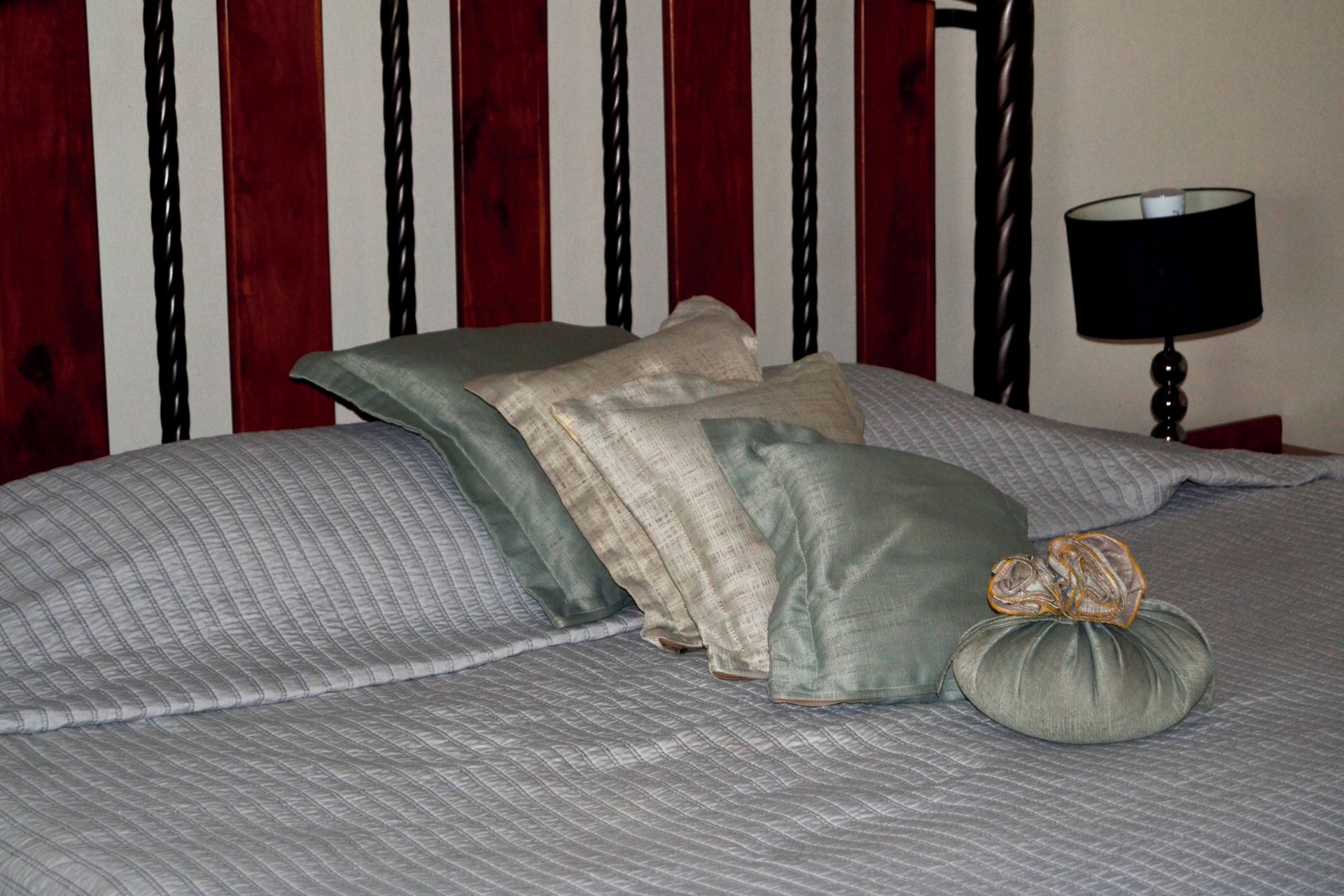 A bed with a grey quilt and pillows, a lamp on a bedside table, and a wooden headboard.