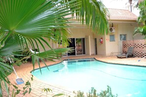 Piscina com deck ladrilhado, área de varanda coberta e muro de tijolos.