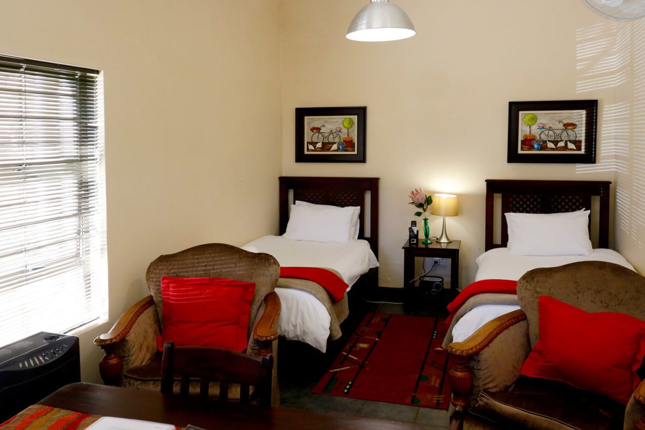 A hotel room with two beds, a sitting area with a chair and a table, a lamp, and artwork on the walls.