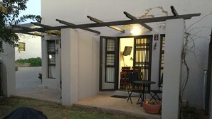 A covered patio with a table and chairs, a potted plant, and a garden with red flowers. - A Little Guesthouse (Bloemfontein)