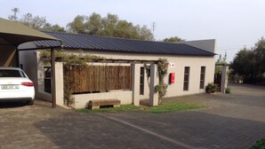 A modern building with a covered entrance, a car parked in front, and a paved driveway. - A Little Guesthouse (Bloemfontein)