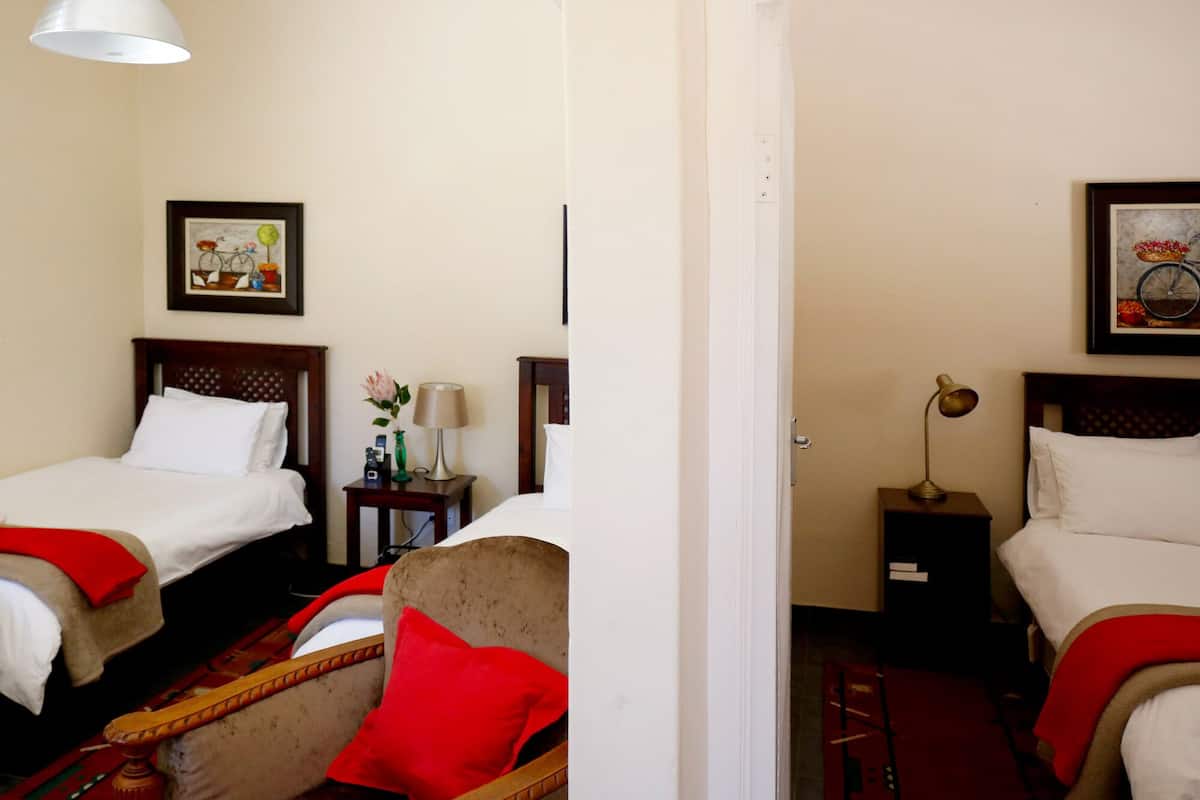 Ein Hotelzimmer mit zwei Betten, einem Sessel, einem kleinen Tisch mit Lampe und einem Bild an der Wand.