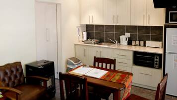 A compact kitchen with a dining table, chairs, a microwave, a toaster, and a refrigerator.