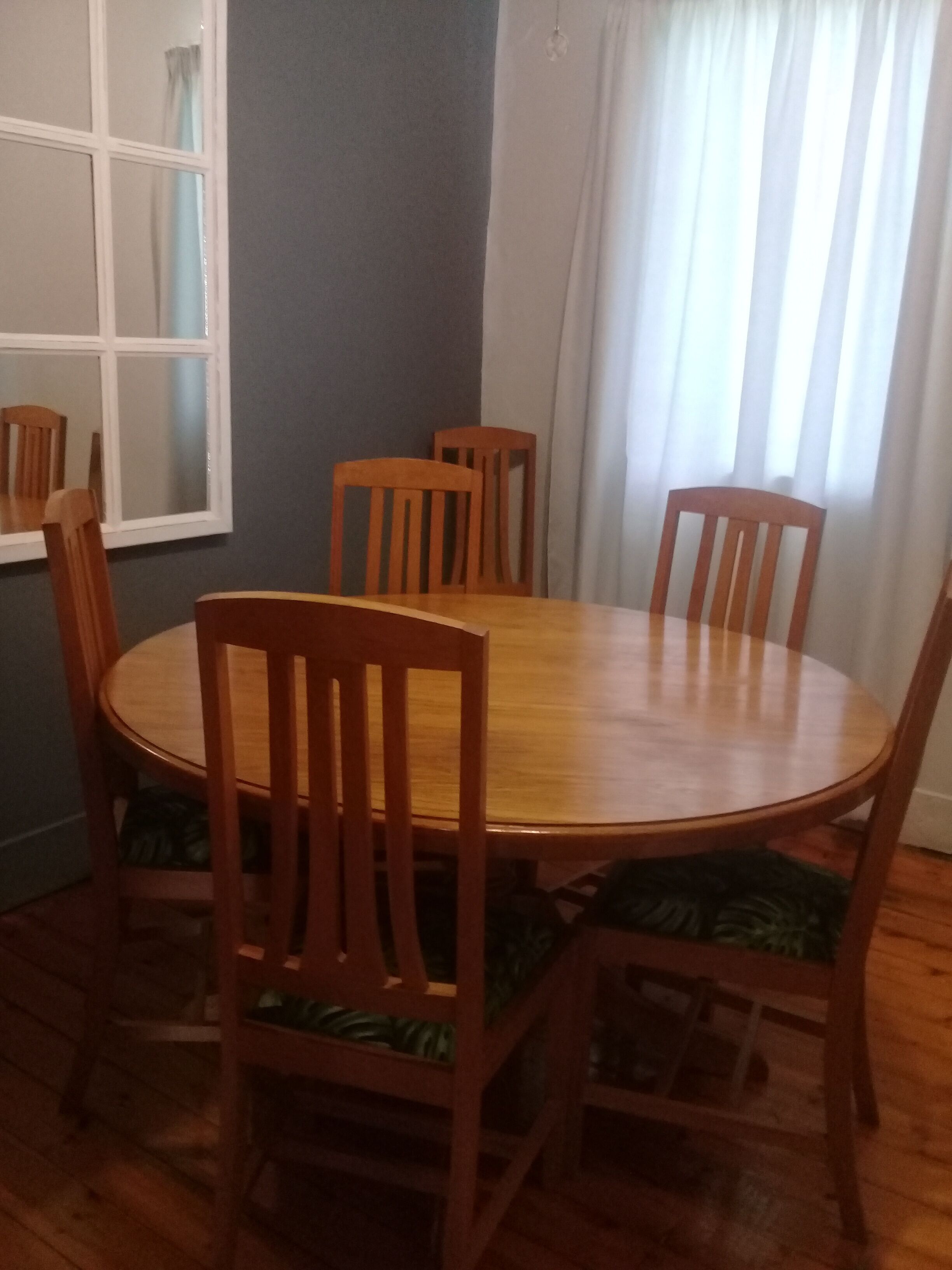 A dining area with a round wooden table surrounded by six wooden chairs with green cushions.