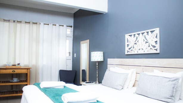 A neatly made bed with a teal blanket, a bedside table with a lamp, and a wall-mounted artwork. - Beechwood B&B (Durban)