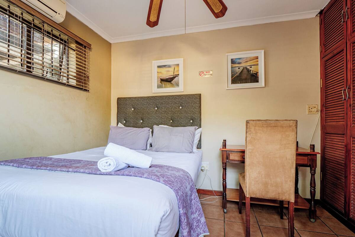 A hotel room with a bed, a desk, and two framed pictures on the wall.