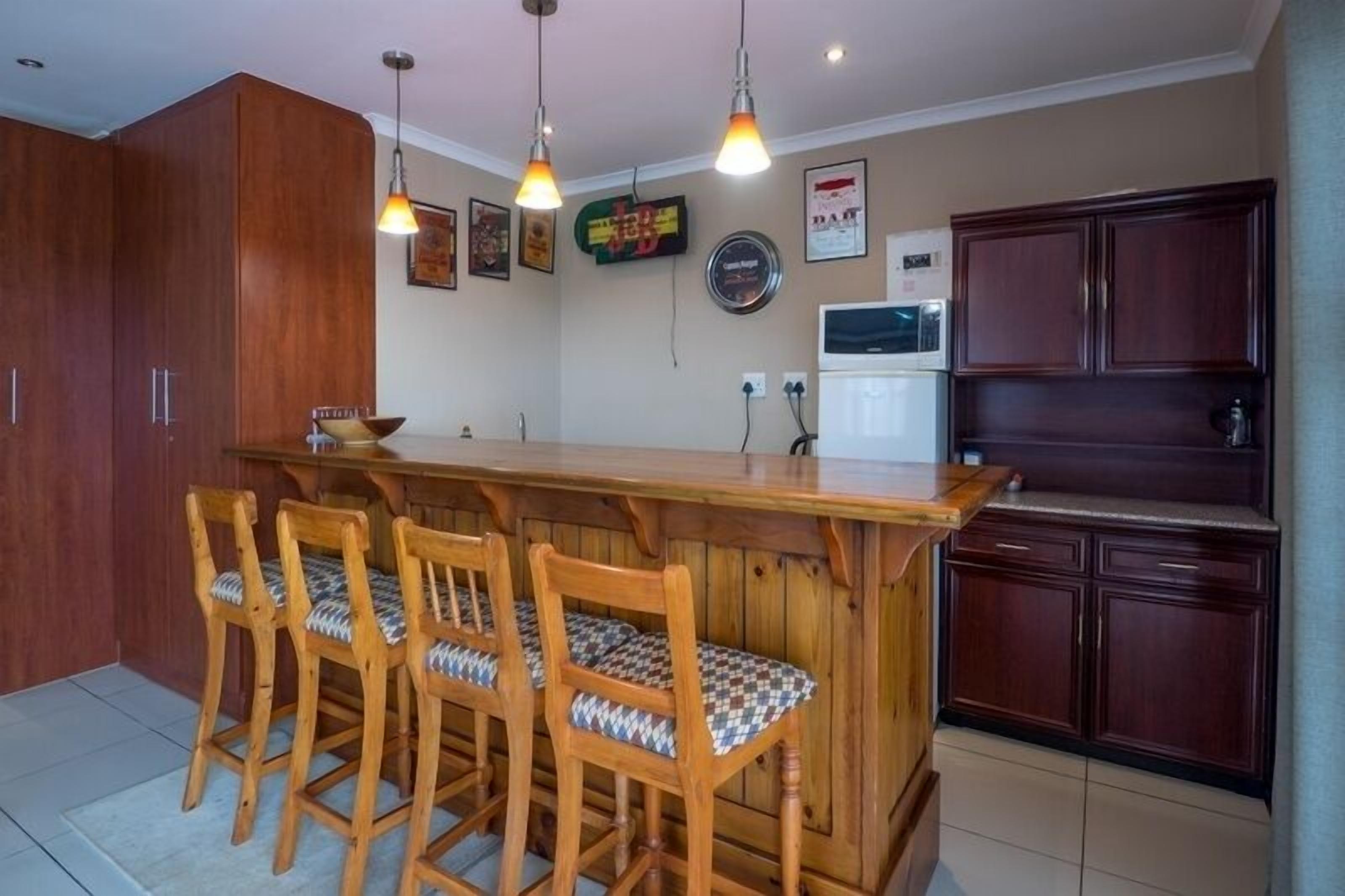 Eine Küche mit Holzausstattung, einer Bar mit vier Stühlen, Pendelleuchten und einem Kühlschrank.