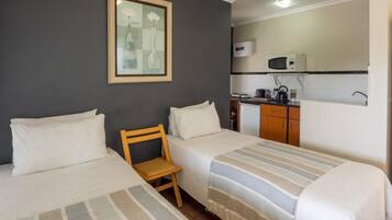 Habitación de hotel con dos camas, una pequeña silla de madera, una kitchenette con microondas, tostadora, hervidor y un lavabo.